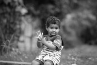 Seorang anak kecil sedang asyik bereksplorasi di taman terbuka sambil menyentuh dedaunan dan rumput basah. Aktivitas alami di luar ruangan ini sangat berguna untuk melatih kecerdasan motorik serta sensorik anak.