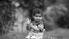 Seorang anak kecil sedang asyik bereksplorasi di taman terbuka sambil menyentuh dedaunan dan rumput basah. Aktivitas alami di luar ruangan ini sangat berguna untuk melatih kecerdasan motorik serta sensorik anak.