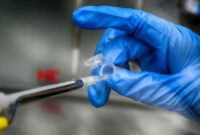 Seorang peneliti medis sedang mengamati sampel rekayasa seluler di laboratorium steril berpenerangan khusus untuk pengembangan terapi gen terapan.