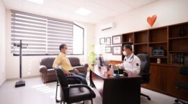 Seorang dokter sedang mendiskusikan keluhan kesehatan fisik dan membaca catatan gejala bersama pasiennya di ruang konsultasi medis.