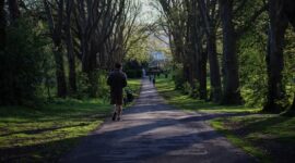 Seorang pekerja berjalan santai di area taman kota untuk meredakan ketegangan pikiran sekaligus menjaga stamina tubuh di sela kesibukan harian.