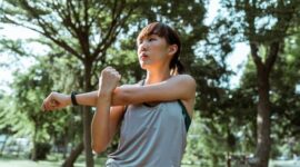 Seorang wanita menikmati kesegaran udara pagi sambil melakukan peregangan ringan di taman kota untuk menjaga kelenturan tubuh dan ketenangan pikiran.