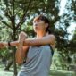 Seorang wanita menikmati kesegaran udara pagi sambil melakukan peregangan ringan di taman kota untuk menjaga kelenturan tubuh dan ketenangan pikiran.