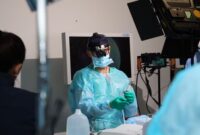 Seorang ahli bedah mengoperasikan lengan robotik presisi tinggi di ruang operasi modern untuk melakukan tindakan medis non-invasif dengan tingkat akurasi maksimal.