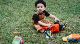 Seorang anak balita sedang asyik bermain tanah dan mengeksplorasi tanaman di halaman terbuka. Aktivitas alami ini berperan penting dalam melatih motorik halus serta memicu rasa ingin tahu sejak dini.