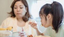 Seorang ibu sedang mendampingi buah hatinya menikmati makanan bergizi dalam suasana yang hangat dan penuh kasih sayang di rumah.