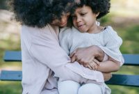 Seorang ibu memberikan dekapan hangat dan mendengarkan keluh kesah anaknya saat beraktivitas bersama di taman kota. Pendekatan pengasuhan bernuansa empati ini membantu anak mengenali serta mengelola emosi mereka secara sehat.