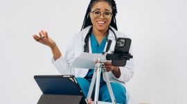 Seorang wanita berkonsultasi secara nyaman dengan dokter spesialis melalui video call di layar ponsel pintar dari ruang tamu rumahnya.
